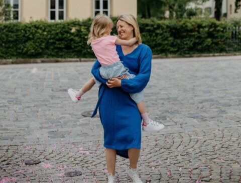Eine Mutter hält ihr Schulkind auf dem Arm. Sie schauen sich in lächelnd an und wirken so, als ob sie sich glücklich im Kreis drehen.